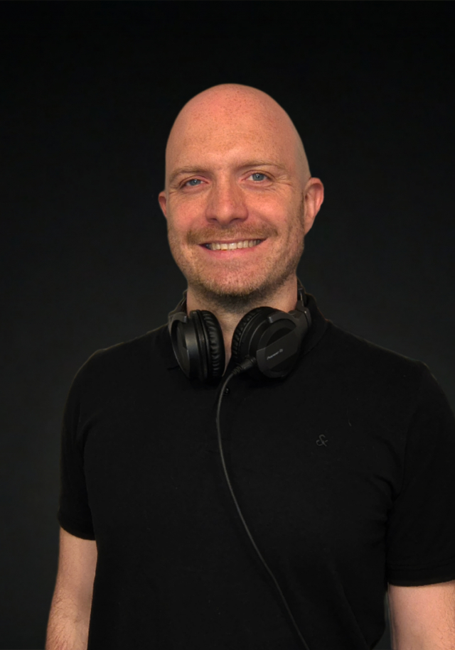 Dad’n’Bass vor dunklem Hintergrund – moderner Techno- und House-DJ mit klarer, kraftvoller Präsenz.